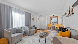 Un salon moderne avec un canapé gris, un fauteuil jaune et une table basse. On y trouve également un coin repas avec une chaise jaune et une table.