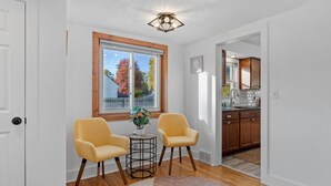 Un salon moderne avec deux fauteuils jaunes, une petite table sur laquelle est posée une plante, et une grande fenêtre donnant sur un paysage automnal.