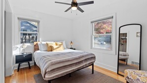 Une chambre à coucher comprenant un lit, une table de chevet, une commode, un miroir et des fenêtres.