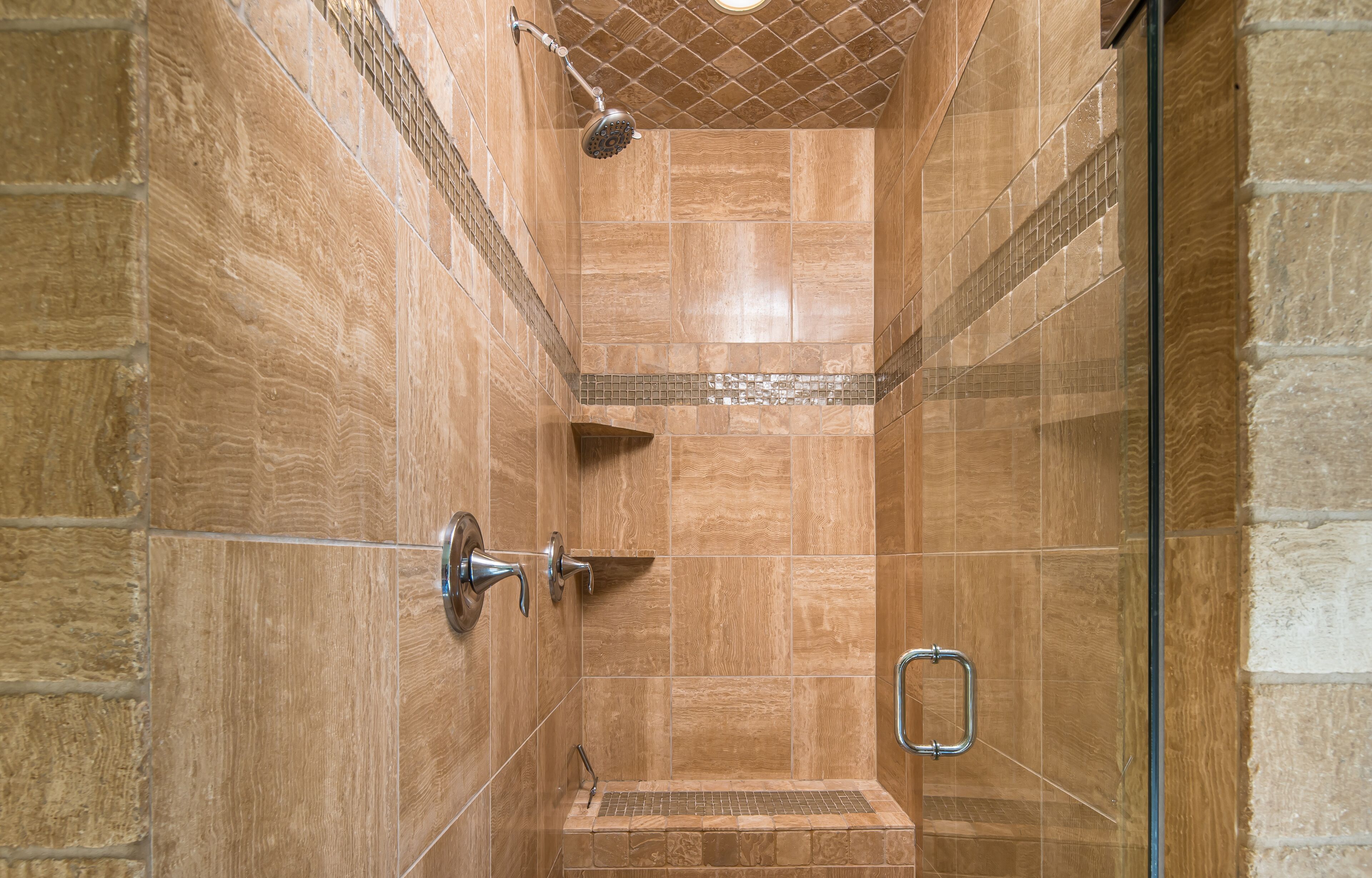 A shower with a glass door, a showerhead, and a tiled wall.