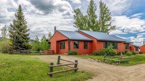 A red building with a metal roof, surrounded by green grass and trees.