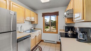 A kitchen with wooden cabinets, a stainless steel refrigerator, a dishwasher, a window with a view of the outdoors, and a coffee maker.