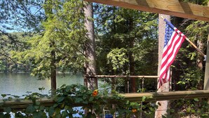 A fenced area with an American flag, a wooden structure, and a view of a lake surrounded by trees.