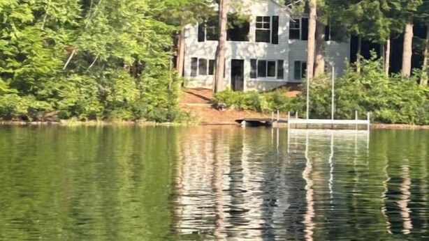 A house surrounded by dense forest, with a dock extending into a calm lake.