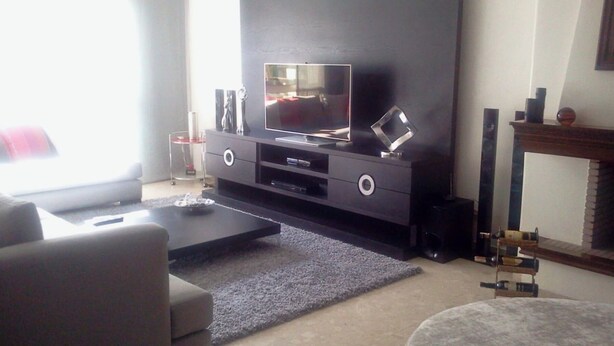Un salon doté d’un grand téléviseur à écran plat posé sur un meuble de télévision en bois foncé, d’un tapis gris, d’une table basse et d’une cheminée avec un manteau de cheminée.