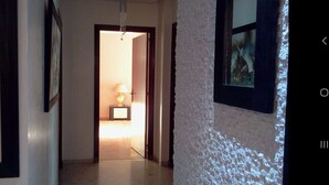 Un couloir avec une porte donnant sur une pièce, un luminaire suspendu et un tableau encadré au mur.