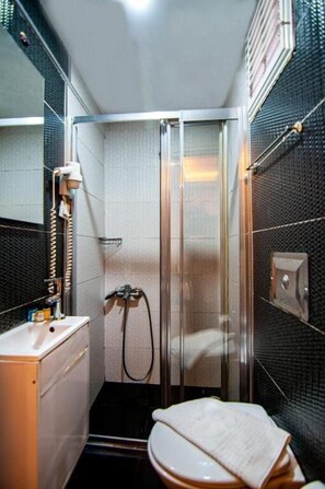 A small, enclosed shower area with a glass door, a sink with a mirror, and a toilet. - Honey Hotel (Istanbul)