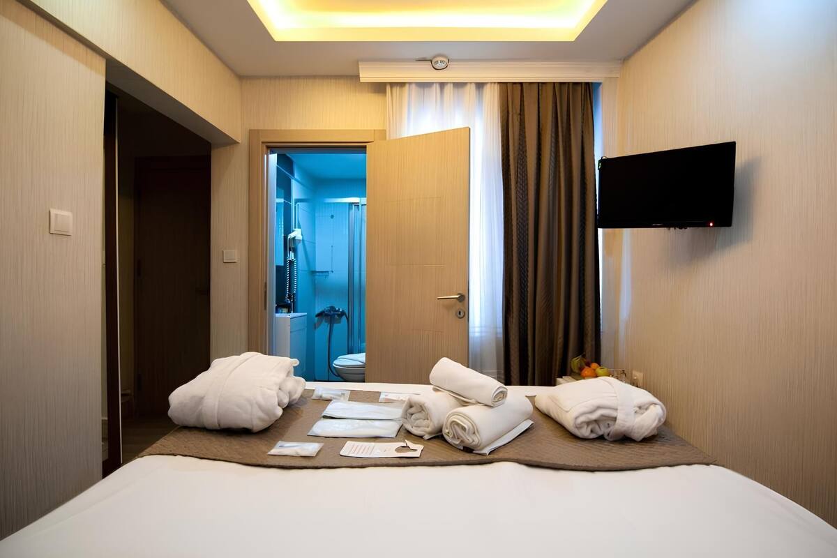 A hotel room with a bed, towels, a TV, and a bathroom visible through an open door.