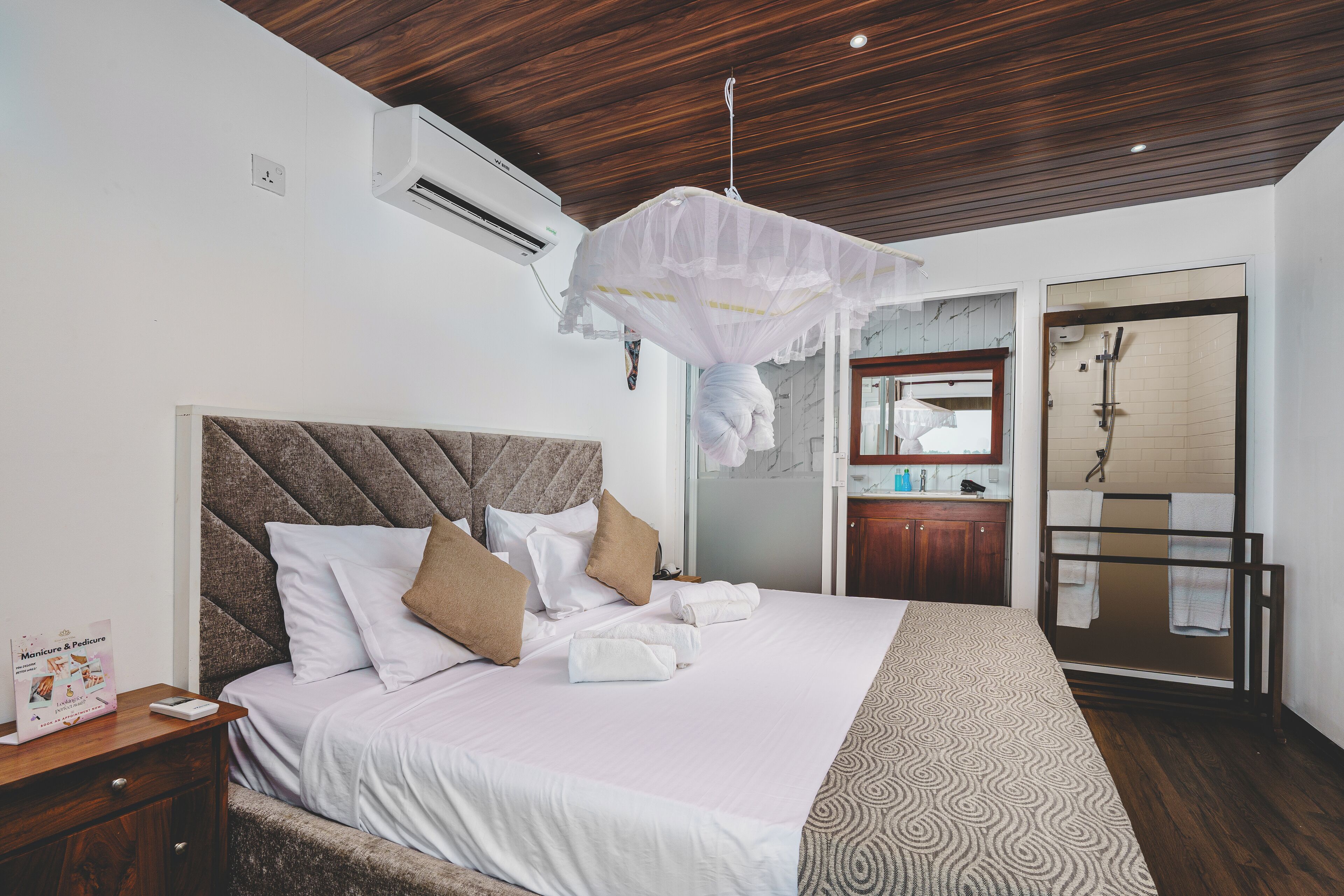 A neatly made bed with white linens and a patterned throw, a wooden headboard, and a hanging mosquito net.