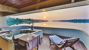 A wooden deck with a hot tub, a table with chairs, and a view of a lake at sunset. - River View Villa (Dharga Town)