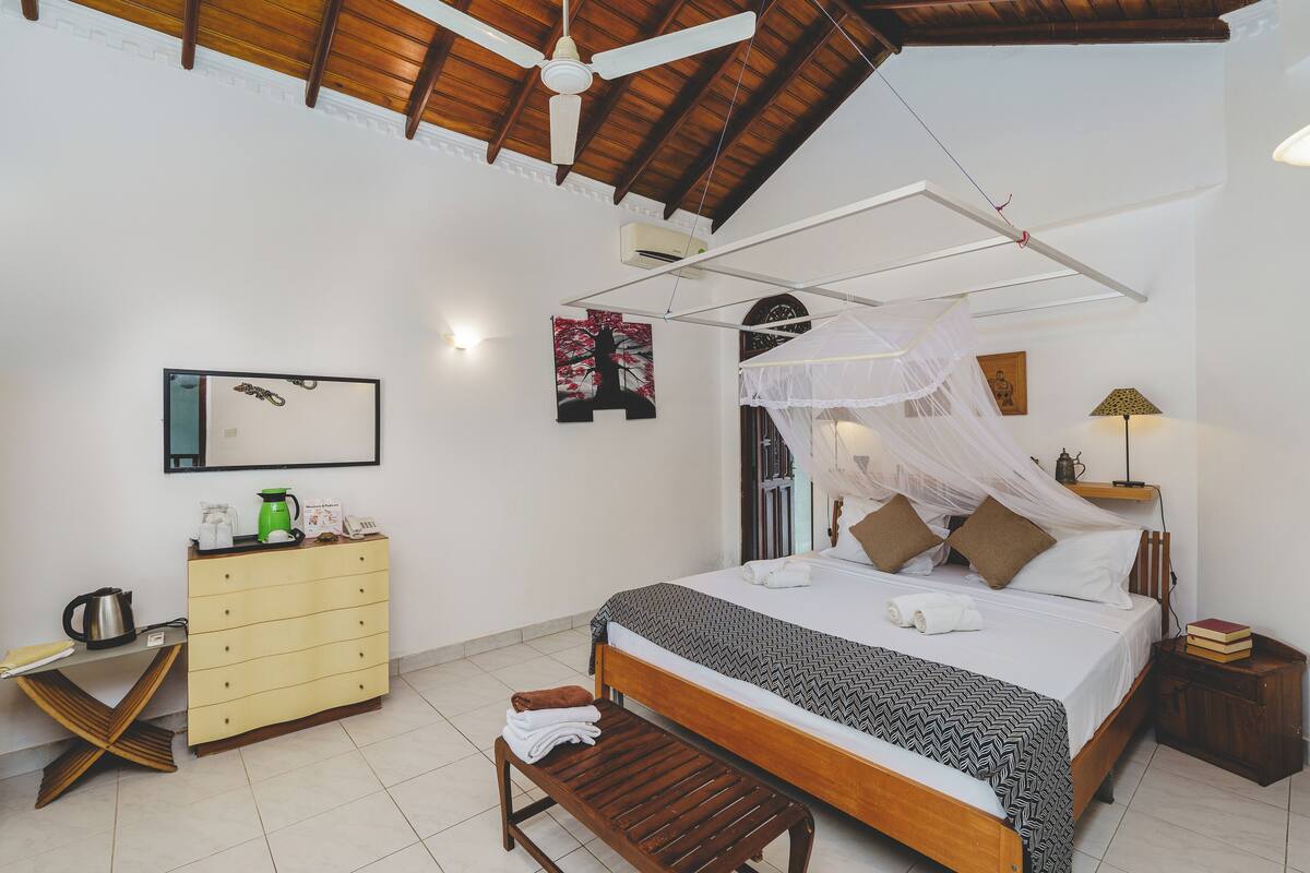 A bedroom with a bed, bedside table, nightstand, wardrobe, and a ceiling fan.