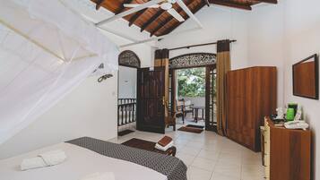 A bedroom with a bed, a wooden wardrobe, a desk with a telephone, and a view of the outside.
