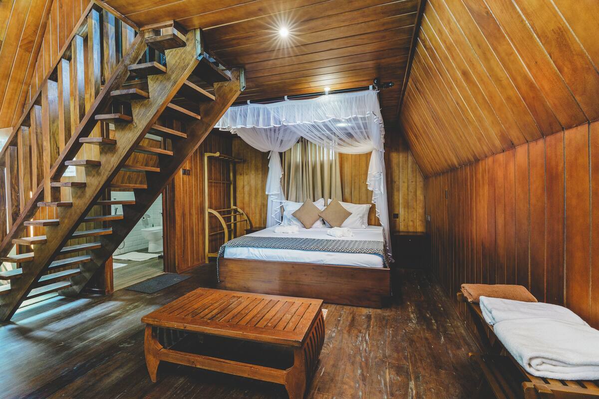 A wooden cabin with a bed, a bench, and a staircase.
