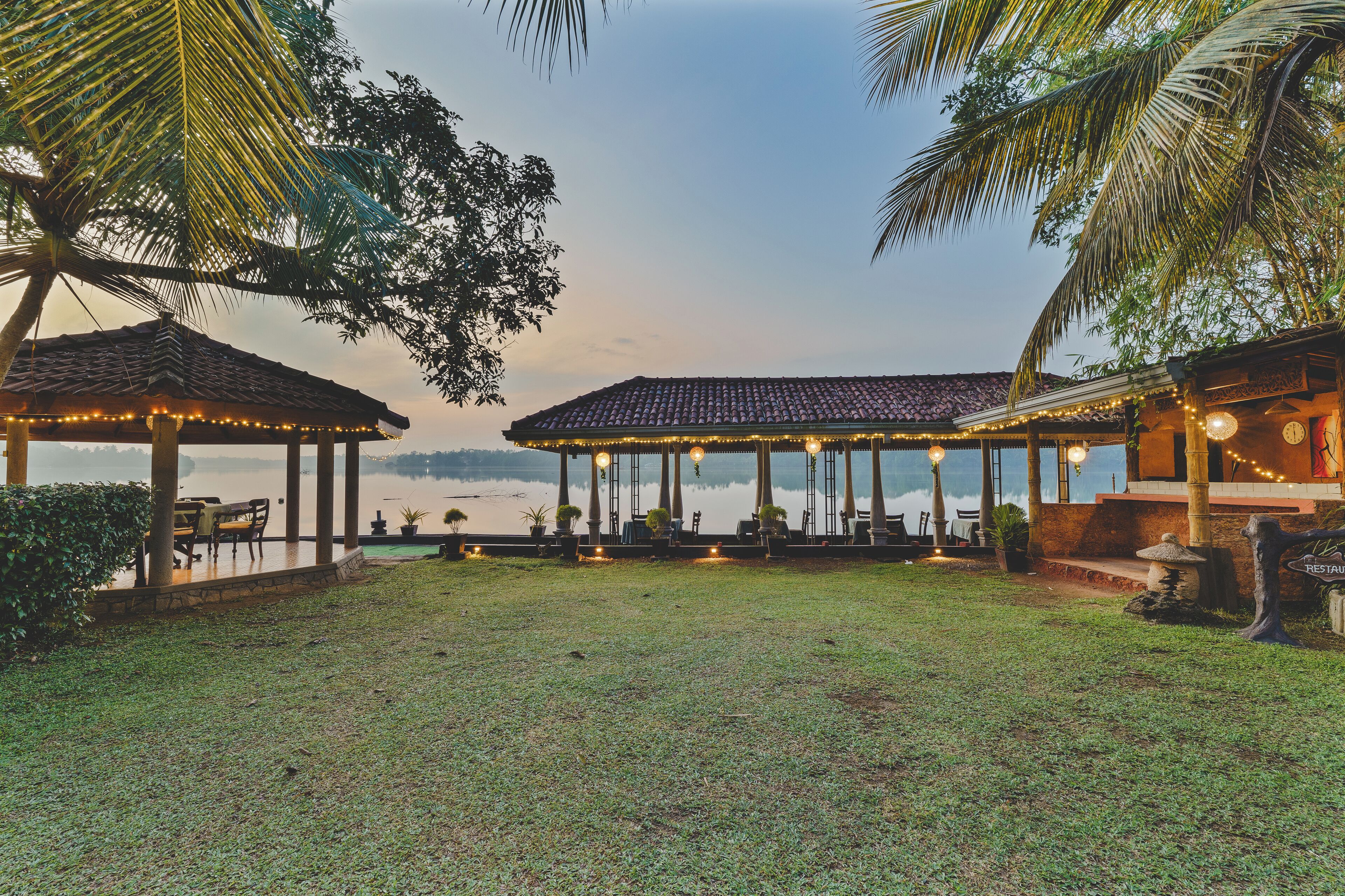 A gazebo with outdoor seating and string lights, overlooking a body of water.