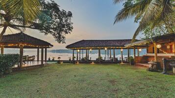 A gazebo with outdoor seating and string lights, overlooking a body of water.