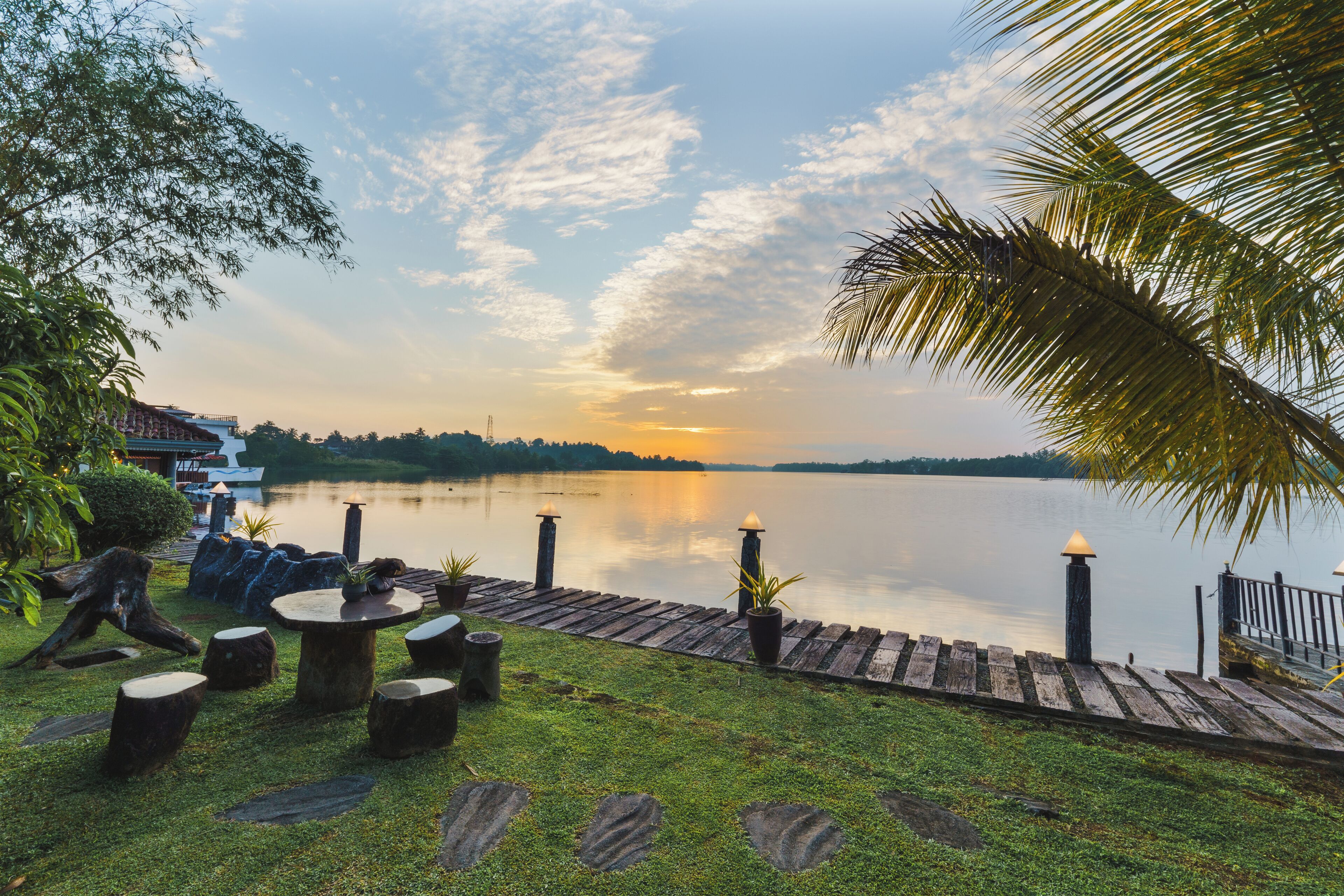 Une terrasse au bord du lac, avec des tables et des chaises en bois, des marches en pierre et une plateforme en bois offrant une vue sur l’eau.