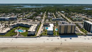An aerial view of a coastal resort with multiple buildings, a beach, and a large pool area. - Ocean Front King Suite #215 (New Smyrna Beach)