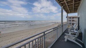 A beach view from a balcony with white Adirondack chairs and a railing. - Ocean Front King Suite #215 (New Smyrna Beach)