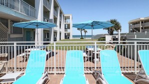 A hotel with a pool area featuring sun loungers and umbrellas, a view of the ocean, and a multi-story building with balconies. - Pool View King Suite #110 (New Smyrna Beach)