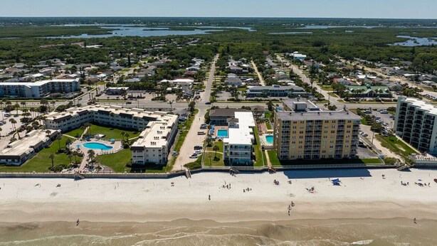 An aerial view of a coastal resort with multiple buildings, a beach, and a large pool area. - Pool View King Suite #110 (New Smyrna Beach)
