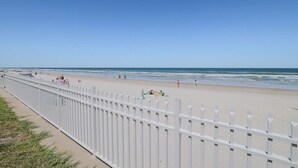 A beach with a white fence, sandy shore, and clear blue sky. - Pool View King Suite #110 (New Smyrna Beach)