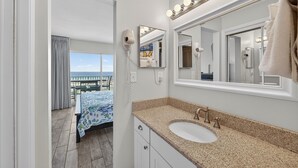 A bathroom with a large mirror, vanity, and a view of the balcony.