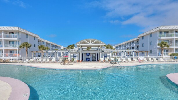 Un hôtel doté d’une piscine centrale, de nombreux balcons et offrant une vue sur un ciel d’un bleu éclatant.