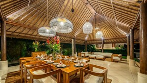 An indoor dining area with a thatched roof, wooden tables, and chairs.