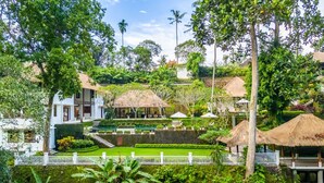 A lush garden with a pond, thatched-roof structures, and a white fence.
