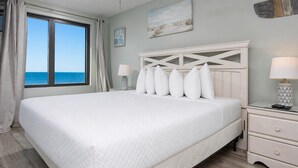 A large bed with a quilted mattress, a bedside table with a lamp, and a view of the ocean through a window. - 2 Bedroom Gulf  Front Located in Gulf Shores (Gulf Shores)