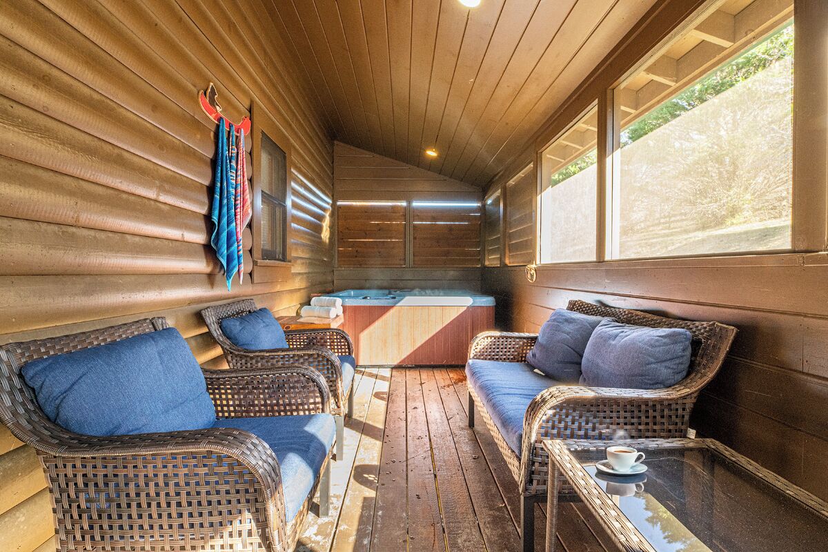 A cozy cabin interior with wicker furniture, a hot tub, and large windows.