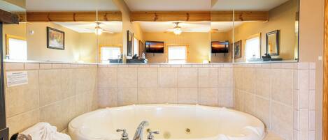 A large, oval-shaped bathtub with two faucets, a showerhead, and a small drain. There are towels on the floor beside the tub.