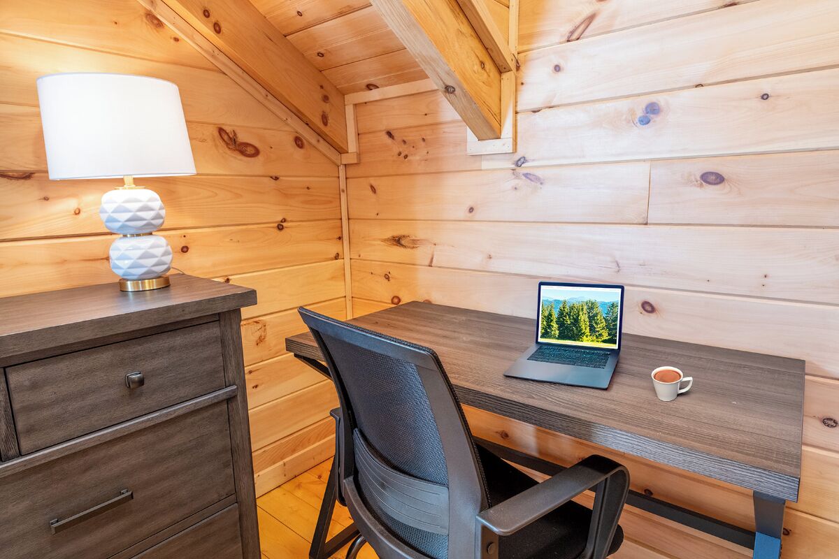 A wooden cabin room with a desk, a laptop, a lamp, and a chair.