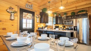 Interior de una cabaña de madera con una mesa de comedor para cuatro personas, electrodomésticos de cocina y un ventanal grande.