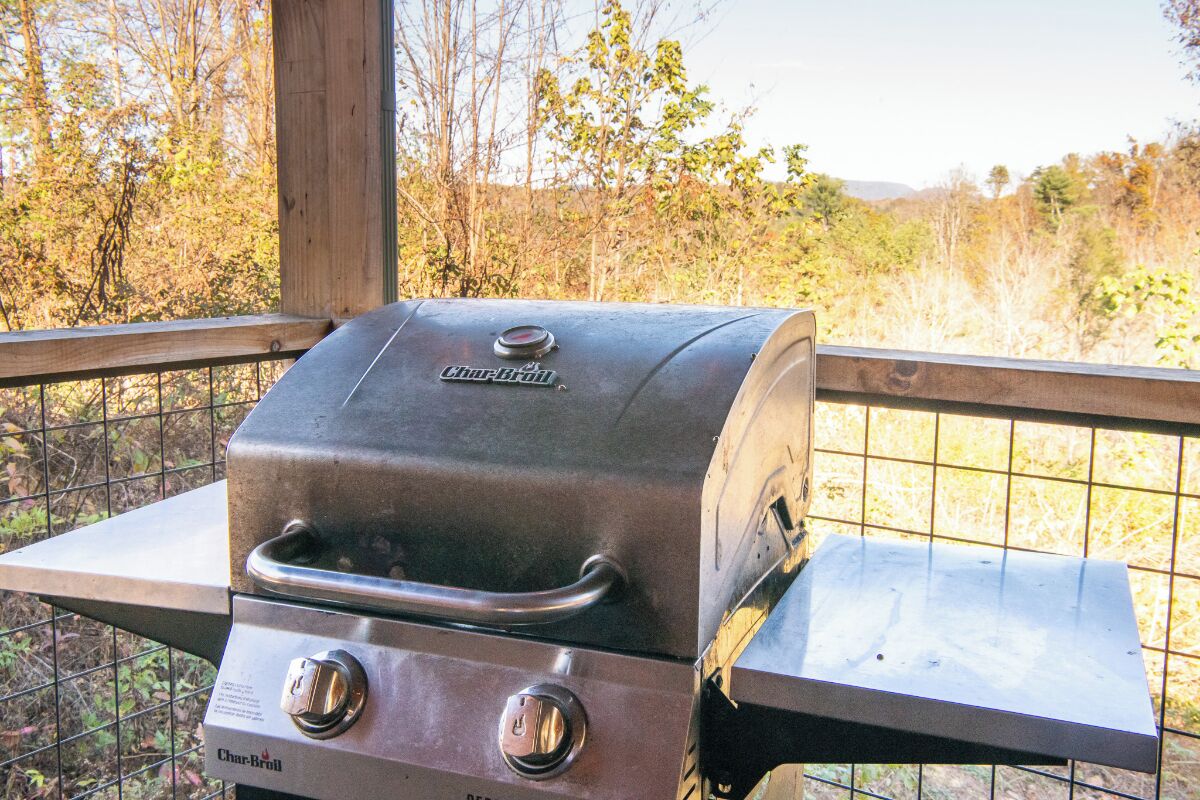 A Char-Broil grill with two control knobs, placed on a table with a metal railing.