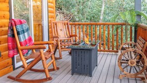 A wooden deck with rocking chairs, a table with a fire pit, and a spinning wheel.