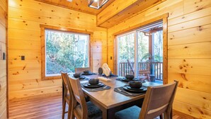 A wooden cabin dining room with a table set for four, large windows, and a view of the outdoors.
