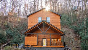 A wooden cabin with a front porch, a small deck, and a pathway leading to the entrance.