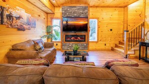 A cozy log cabin interior with a fireplace, a large flat-screen TV, and a comfortable seating area.