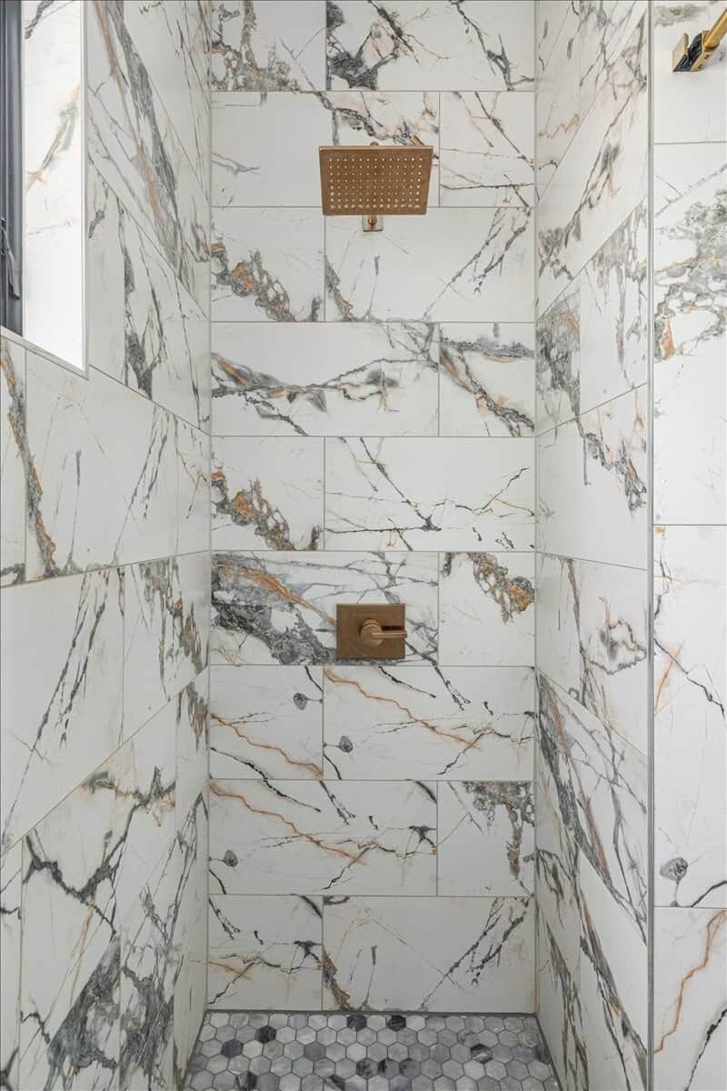 Une douche avec des carreaux de marbre et un pommeau de douche en métal.