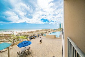 A rooftop pool area with lounge chairs, a barbecue grill, and a view of the beach and ocean.