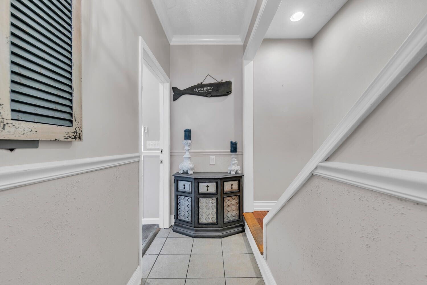 A hallway with a white door, a decorative fish-shaped sign, and a dark wooden console with drawers.