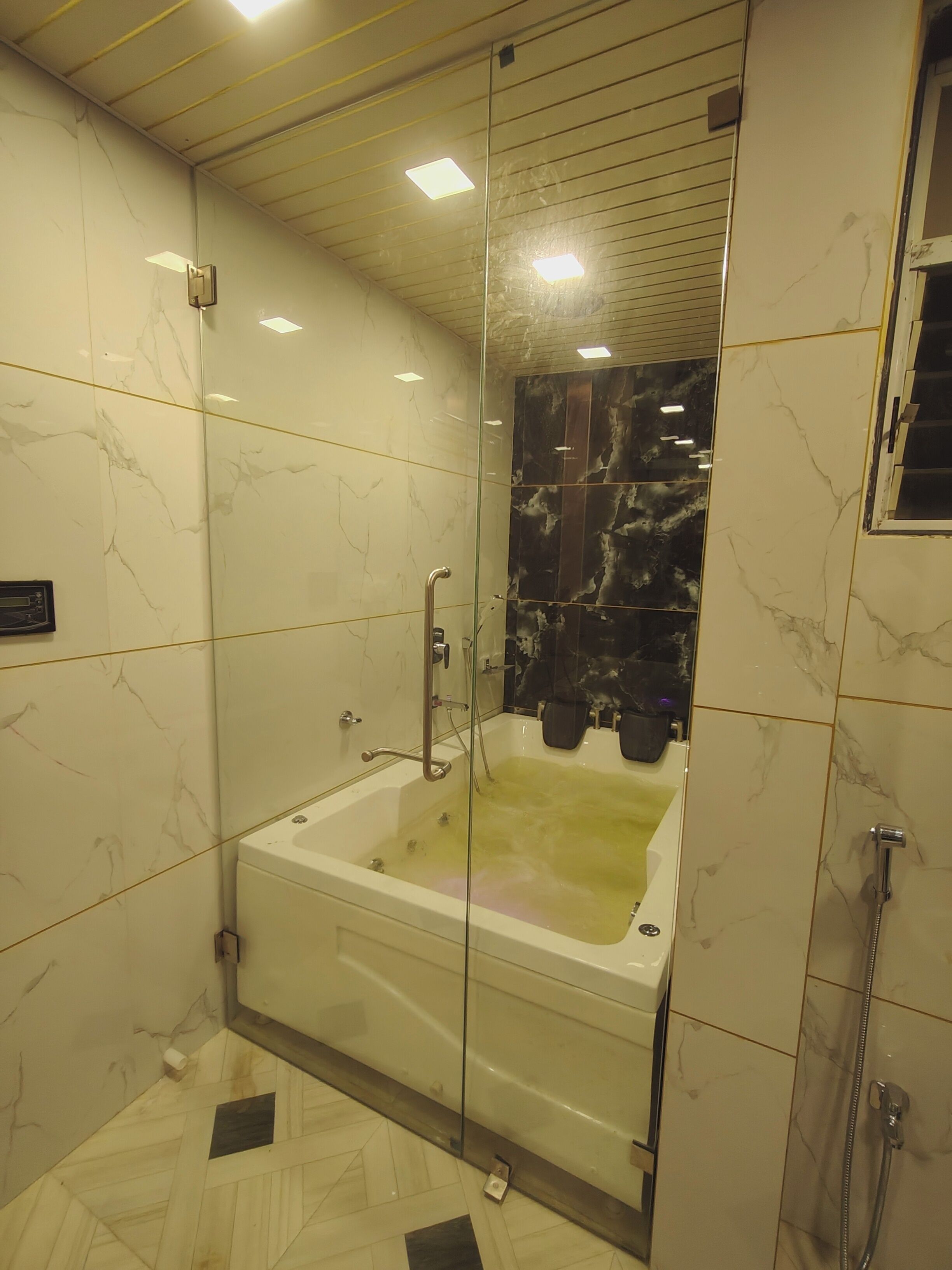 A modern bathroom with a glass-enclosed bathtub, marble walls, and a tiled floor.