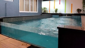Ein Schwimmbecken mit einer schilfernden Kante, einer Holzterrasse und einer Wand mit vertikalen Streifen.