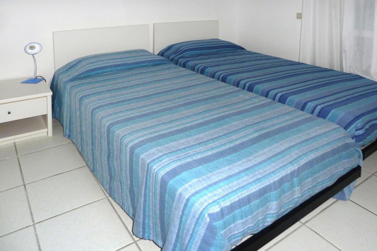 A room with two beds, a nightstand, and a lamp.