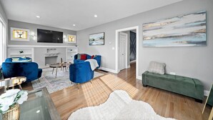 Ein modernes Wohnzimmer mit Kamin, blauen und grünen Sofas, einem Flachbildfernseher und Kunstwerken an den Wänden.