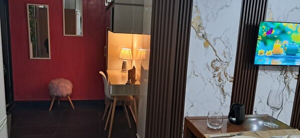 A modern hotel room with a dining area, a TV mounted on the wall, and a marble-patterned wall.