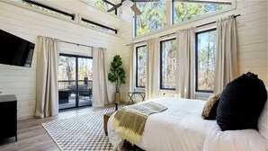 Un dormitorio con una cama grande, un ventilador de techo y vistas al exterior a través de varias ventanas.