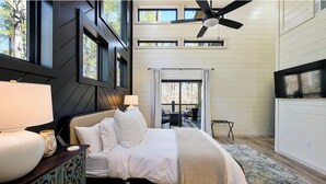 Un dormitorio con cama, lámparas de noche, ventilador de techo y vistas a una terraza exterior.