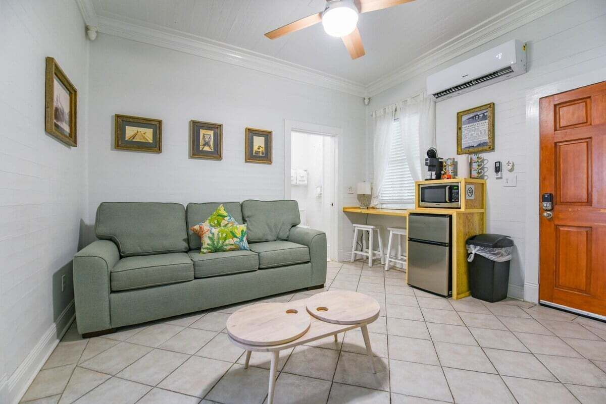 A compact living space with a sofa, two round tables, a kitchenette, and a ceiling fan.